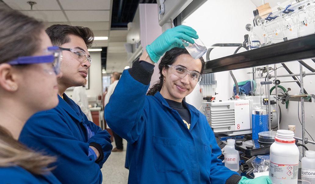 Students in lab coats examining a sample in a university chemistry lab
